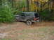 1988 Ford Bronco - A dirty black Ford Bronco navigates a wooded trail during autumn.
