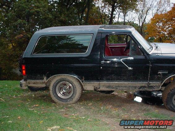 Black Ford Bronco parked on grassy area, side view. Red interior visible