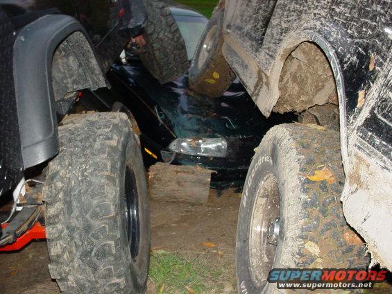 Mud-covered off-road tires and fenders of multiple vehicles in a tight, muddy scene