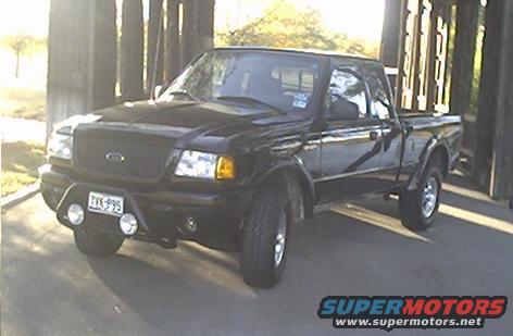 Black 2002 Ford Ranger pickup truck with aftermarket bumper and lights, parked under a bridge