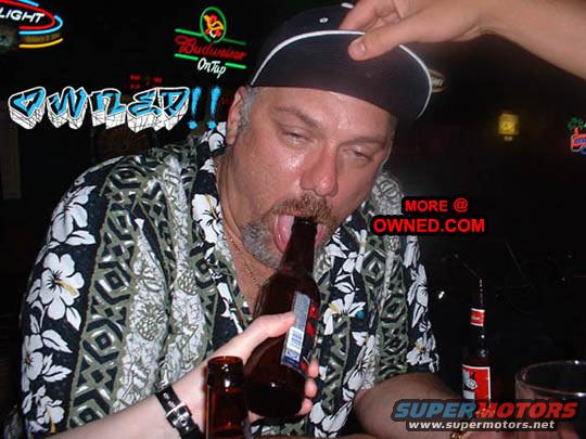 Man with a black baseball cap and floral shirt drinks from a beer bottle in a bar with neon signs