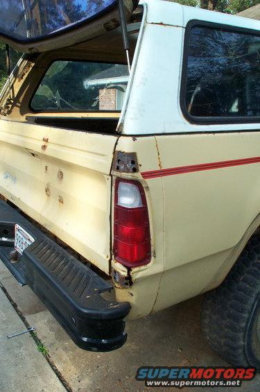Cream pickup truck rear quarter panel with red stripe and white camper shell
