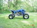 2004 Yamaha YFZ450 - A blue Yamaha YFZ450 ATV is shown from the side, parked on a grassy area with trees in the background.
