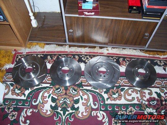 Four brake rotors laid out on a patterned rug. Two are slotted, two are plain