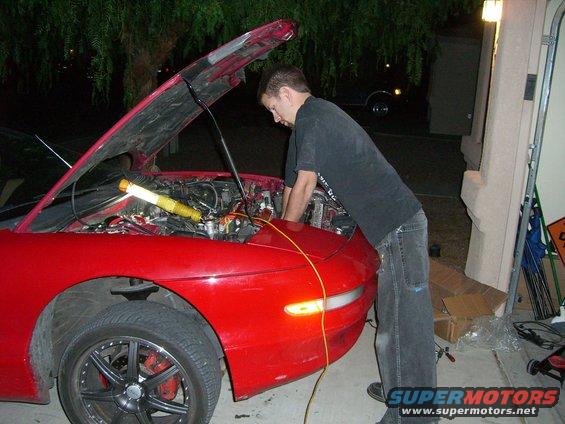 Red car front view, hood open, mechanic working on engine
