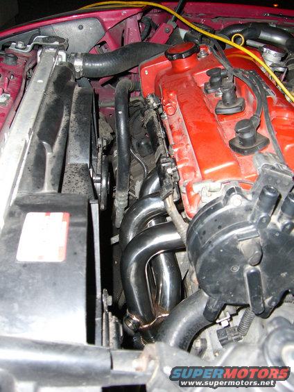 Engine bay showing a red valve cover, exhaust manifold, radiator, and fan