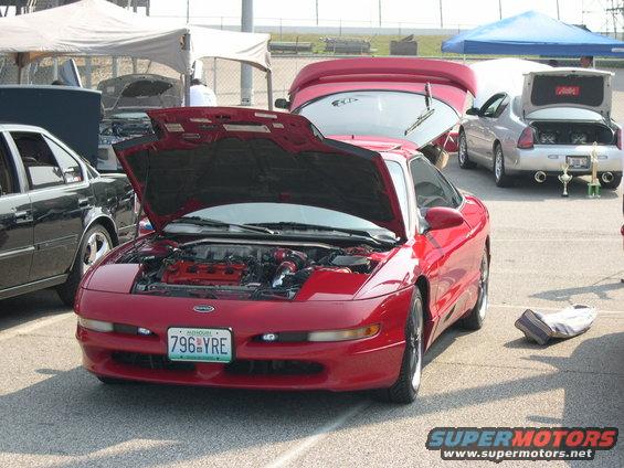 red 1997 Ford Probe with hood open, showing engine. Other cars and tents in background