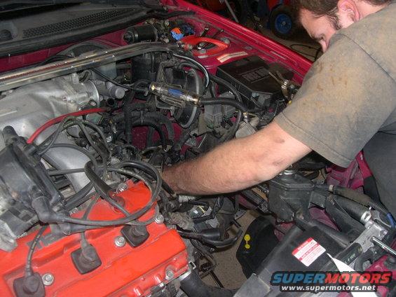 Mechanic working on 1997 Ford Probe engine bay, red valve cover visible