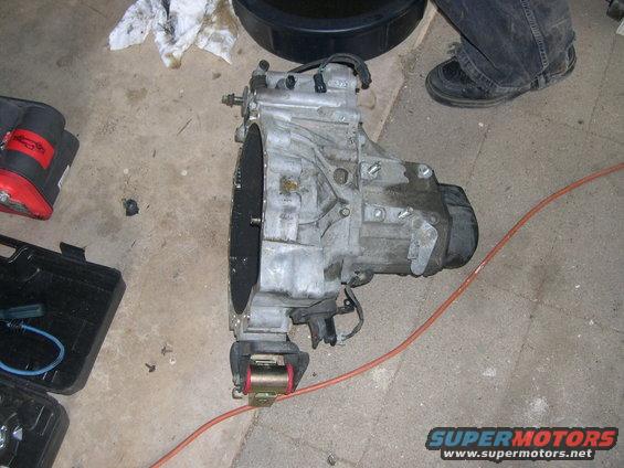 Car transmission with red and gold mount, on concrete floor with tools