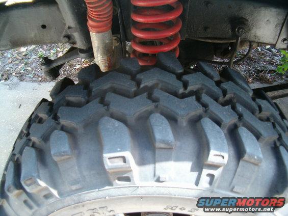 Close-up of a large, knobby off-road tire with a red coil spring and shock absorber visible above it