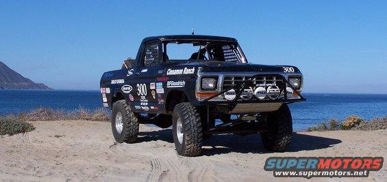 Black 1979 Ford Bronco with racing decals and off-road tires parked on a sandy beach