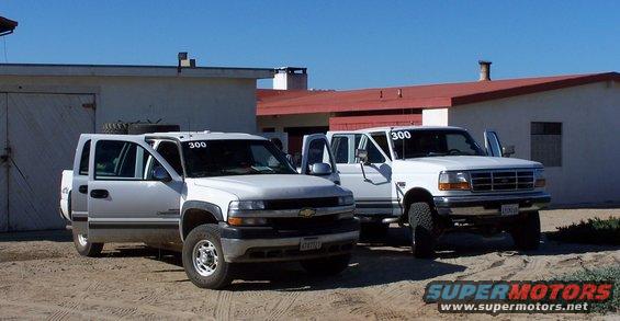Two white pickup trucks parked outside buildings, one with doors open