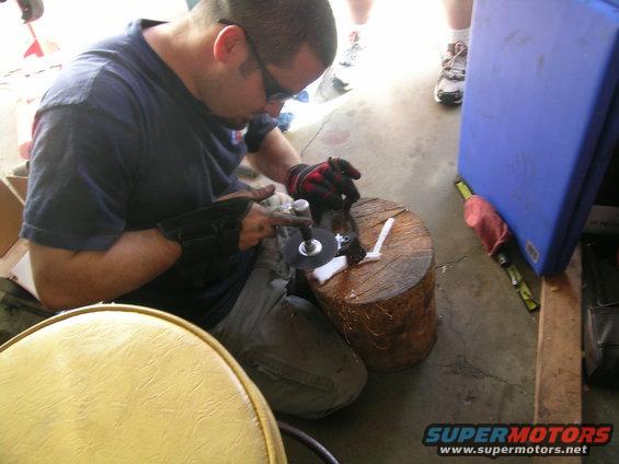 Man wearing gloves and safety glasses grinds a metal part on a wooden block