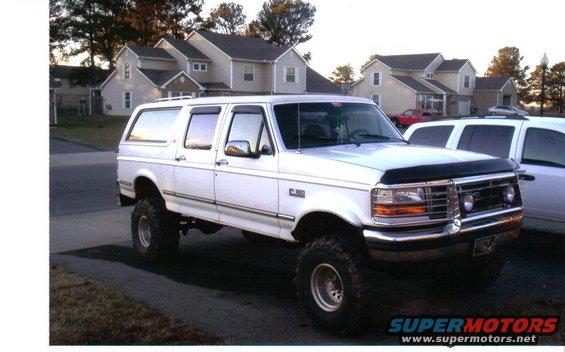 White extended SUV with lifted suspension, aftermarket wheels, and a black bug deflector. Visible "F-250" badge on fender