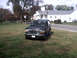 1996 Ford Bronco - A dark blue Ford Bronco is parked on a grassy area with a building and trees behind it.
