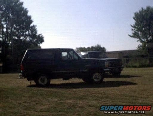 Dark blue Ford Bronco parked on grass, side view. Another vehicle is behind it