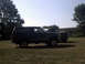 1996 Ford Bronco - A dark blue Ford Bronco is parked on a grassy field next to another vehicle under a clear sky.