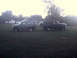 1996 Ford Bronco - Two dark green Ford Broncos are parked on a grassy field with houses and trees in the background.