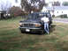 1996 Ford Bronco - A person leans against a dark green 1996 Ford Bronco parked on a grassy area next to a road.