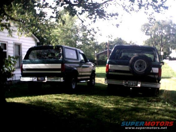 Two dark green SUVs with silver trim parked in a grassy yard. One has a spare tire mounted on the rear door