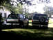 1996 Ford Bronco - Two SUVs are parked in a yard on a sunny day, with trees and a house in the background.