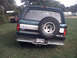 1996 Ford Bronco - A dark green Ford Bronco is parked on grass with another red vehicle in the background.