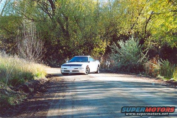 1996 Ford Probe parked on a dirt road with trees in the background