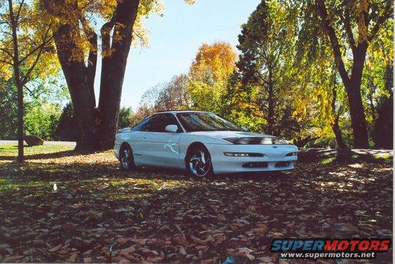 White 1996 Ford Probe parked on fallen leaves, trees with yellow and orange foliage in background