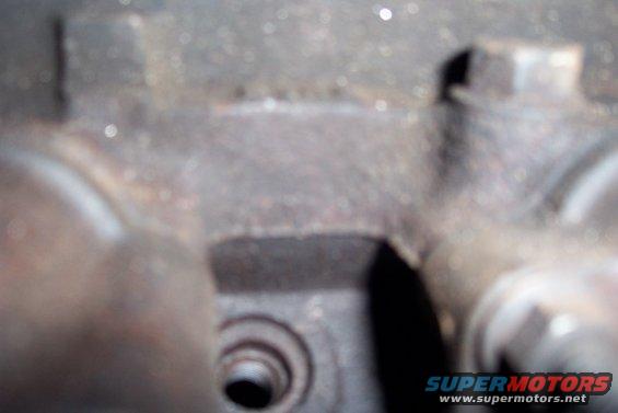 Close-up of a rusty, metallic engine component with visible bolt heads and a threaded hole