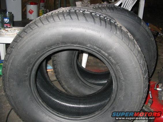 Four black tires stacked, with visible tread patterns and sidewall text