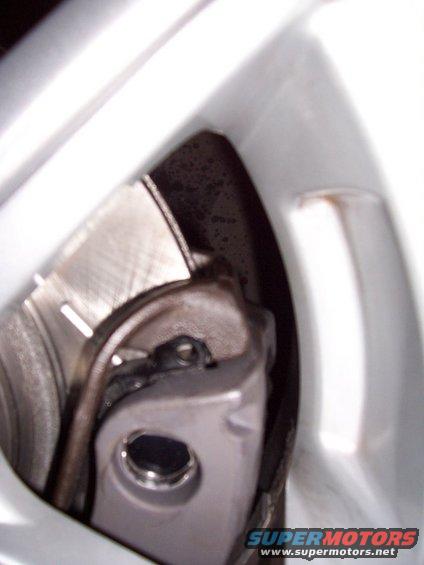 Close-up of a car's brake caliper and rotor assembly, partially obscured by a white wheel rim