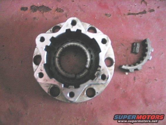 Damaged metal hub assembly with a broken gear piece next to it on a red surface