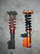 1996 Ford Probe - Comparison of two different car suspension strut assemblies, one appears older and worn, the other is a newer aftermarket part.