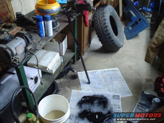 Workbench with spray paint cans, vise, tire, and black painted parts on newspaper