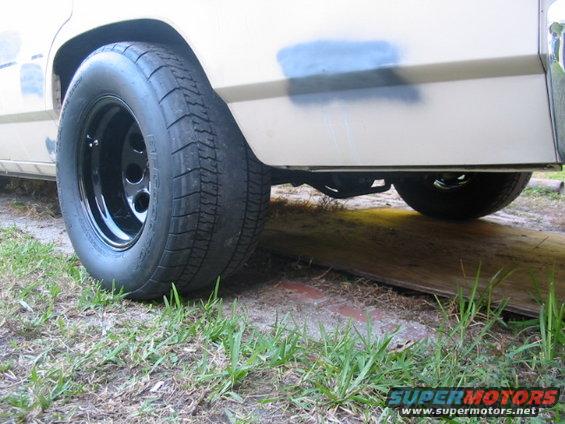Rear wheel with black rim and drag radial tire on a white vehicle with a blue spray-painted patch on the fender