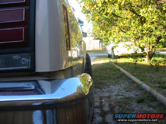 Rear quarter panel and bumper of a car with a lemon tree and another car in the background