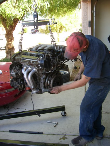 Red car hood and fender with a V6 engine being lifted by a hoist