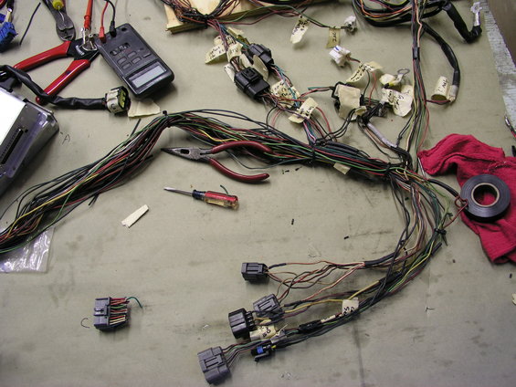 Automotive wiring harness spread out on a table with tools including pliers, a multimeter, and a screwdriver