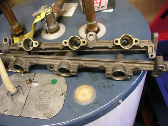 Two metal fuel rails resting on top of a blue water heater