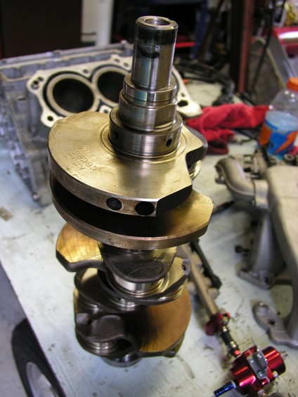 Crankshaft with "KENT CGE200" visible, resting on a workbench with engine block and parts