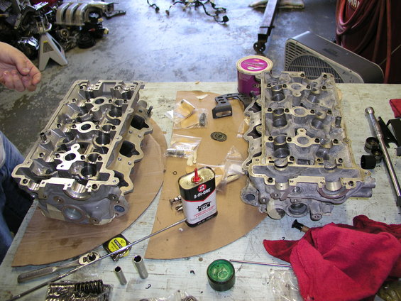 Two engine cylinder heads disassembled on a workbench with various tools and small parts