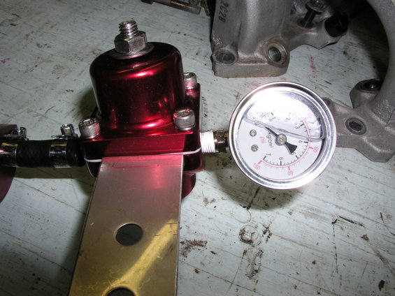 Red fuel pressure regulator with attached gauge, mounted on metal bracket
