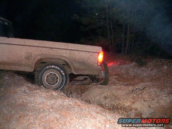 Muddy pickup truck driving off-road at night, rear view showing taillight and tire