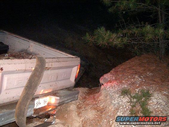 White Ford F-Series truck rear, stuck on rocky terrain at night