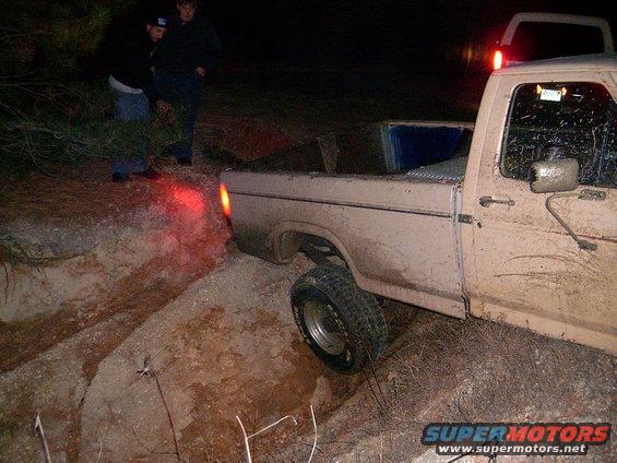 Pickup truck with one wheel in a ditch, people nearby at night