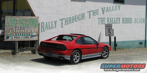 Red 1986 Pontiac Fiero parked in front of a building with mural