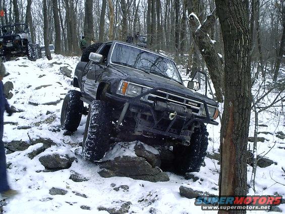 Black Toyota 4Runner with big tires climbing rocks in the snow. Another Jeep is visible behind it