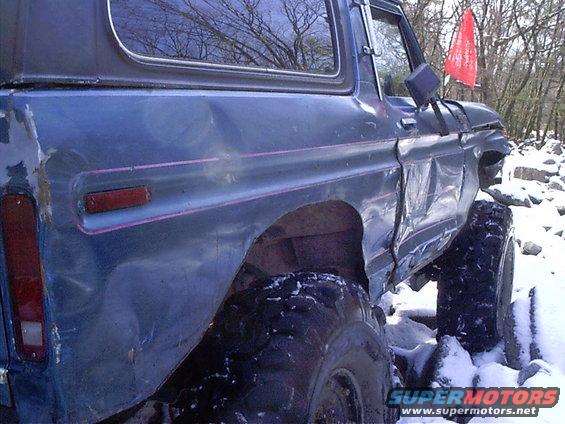 Blue SUV, looks like a Bronco, with heavy body damage and large off-road tires, parked in snow
