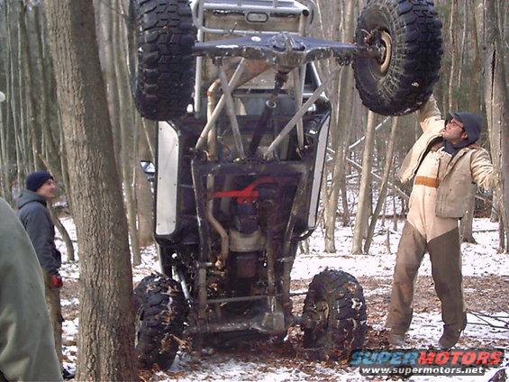 Off-road buggy flipped upside down in a snowy wooded area with people around