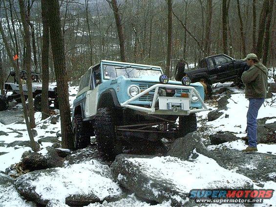 Light blue and white off-road SUV with a winch and brush guard navigating rocks and snow